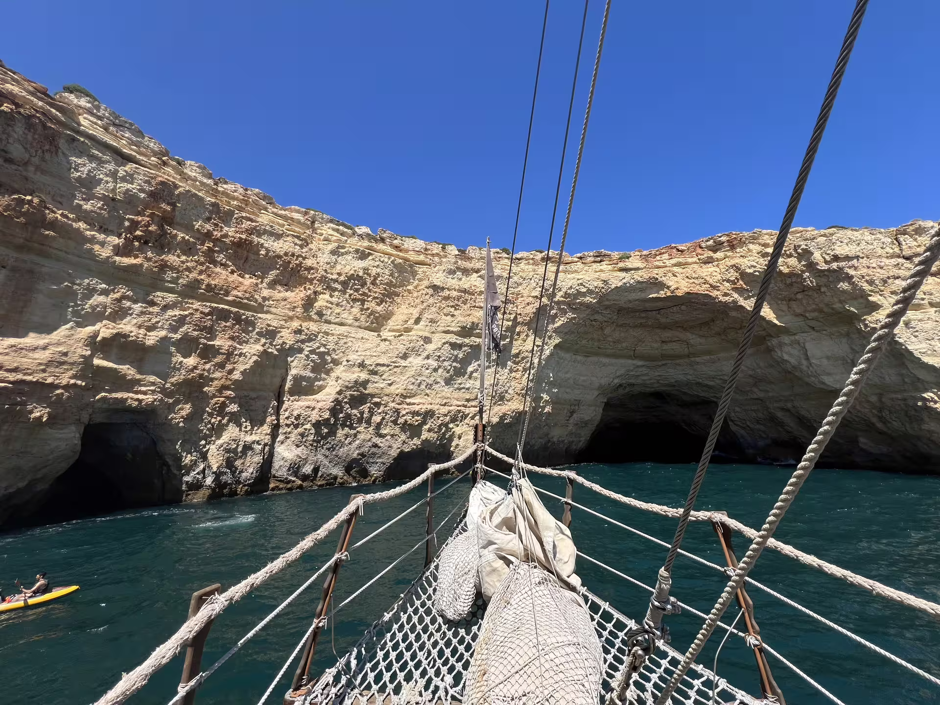 View from the ship's bow approaching the stunning Benagil caves, with clear blue skies and rocky cliffs.