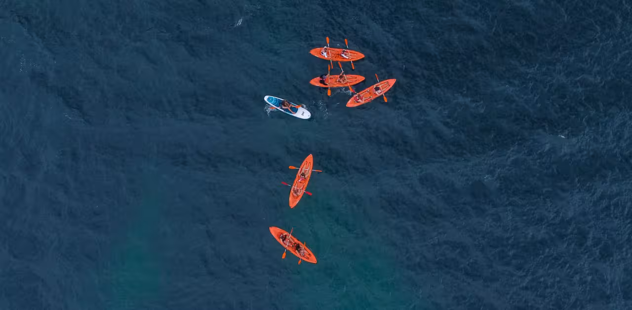 Aerial view of orange kayaks and a paddleboard touring deep blue Atlantic waters on a Benagil Caves sunrise adventure