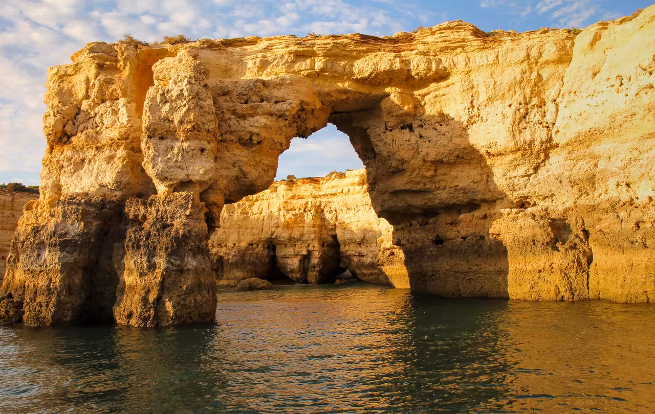 Golden limestone rock arch rising from calm sea waters on Algarve Benagil sunset boat tour from Albufeira