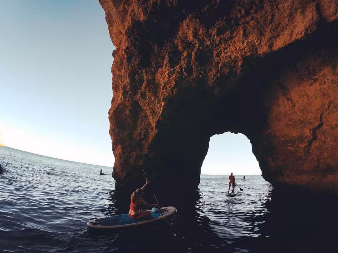 Paddleboarders explore Benagil sea caves at sunset, gliding through natural rock arches on a guided Algarve SUP tour