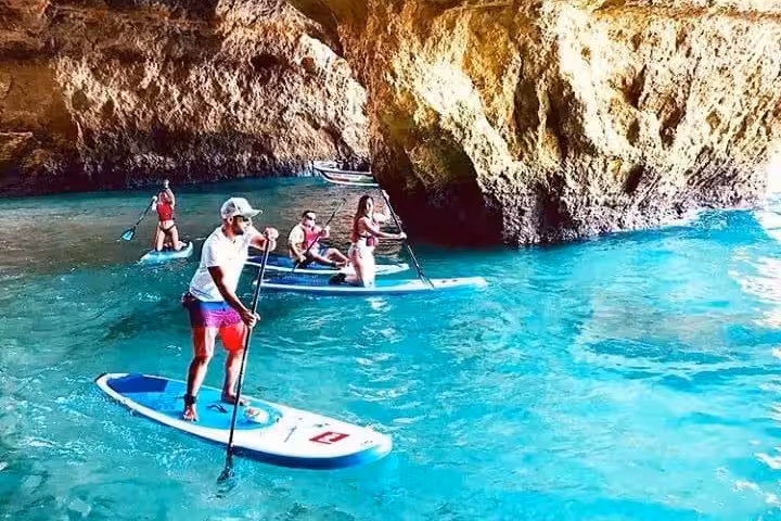 Group of travelers on stand up paddleboards exploring turquoise water inside Benagil Caves on a guided Algarve sunset tour