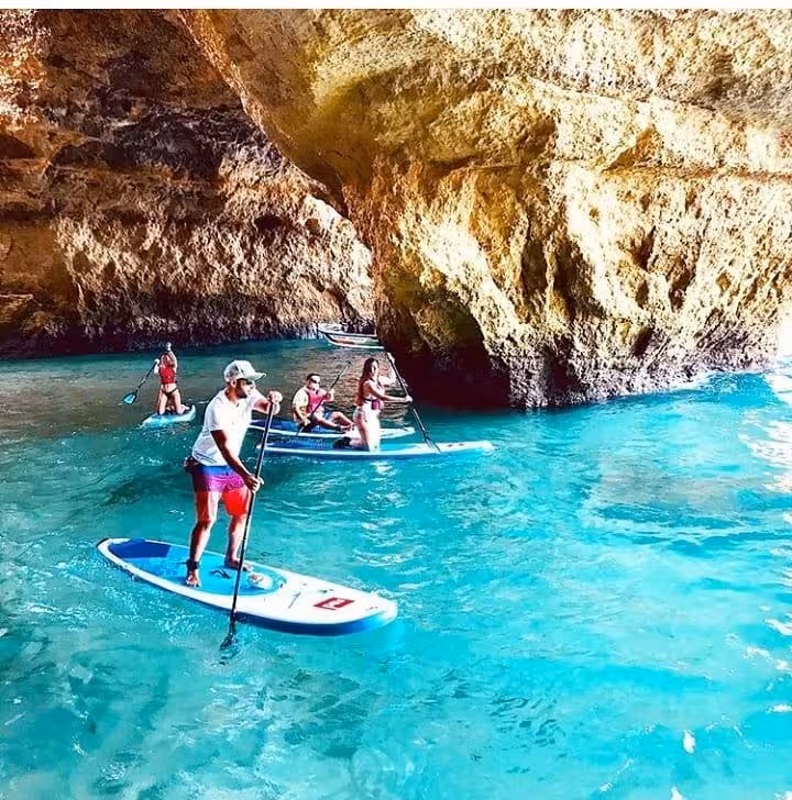 Group of travelers on stand up paddleboards exploring turquoise water inside Benagil Caves on a guided Algarve sunset tour