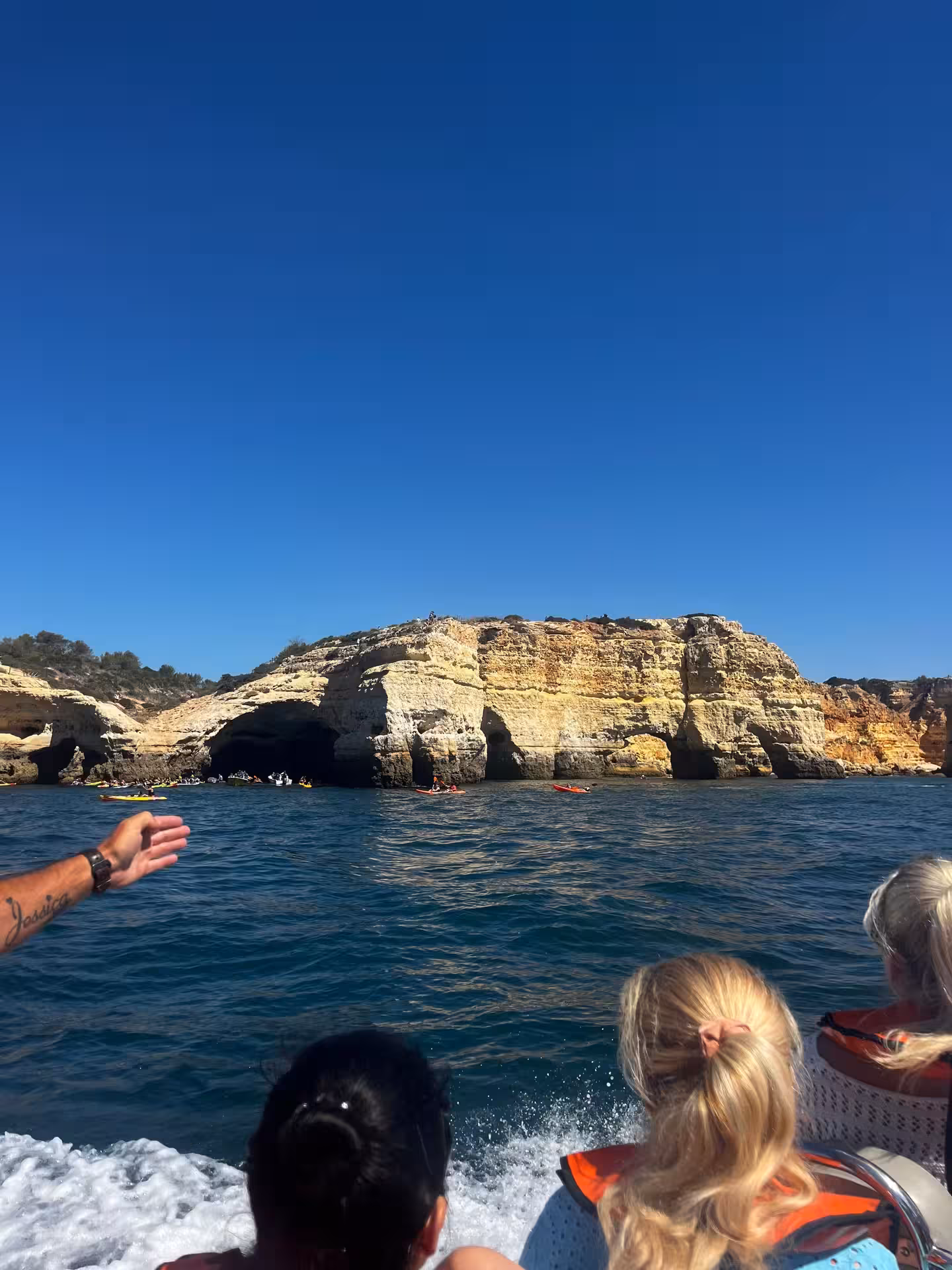 Visitors on Benagil & Dolphins Tour speedboat admiring Algarve coastline cliffs and sea caves under clear blue sky