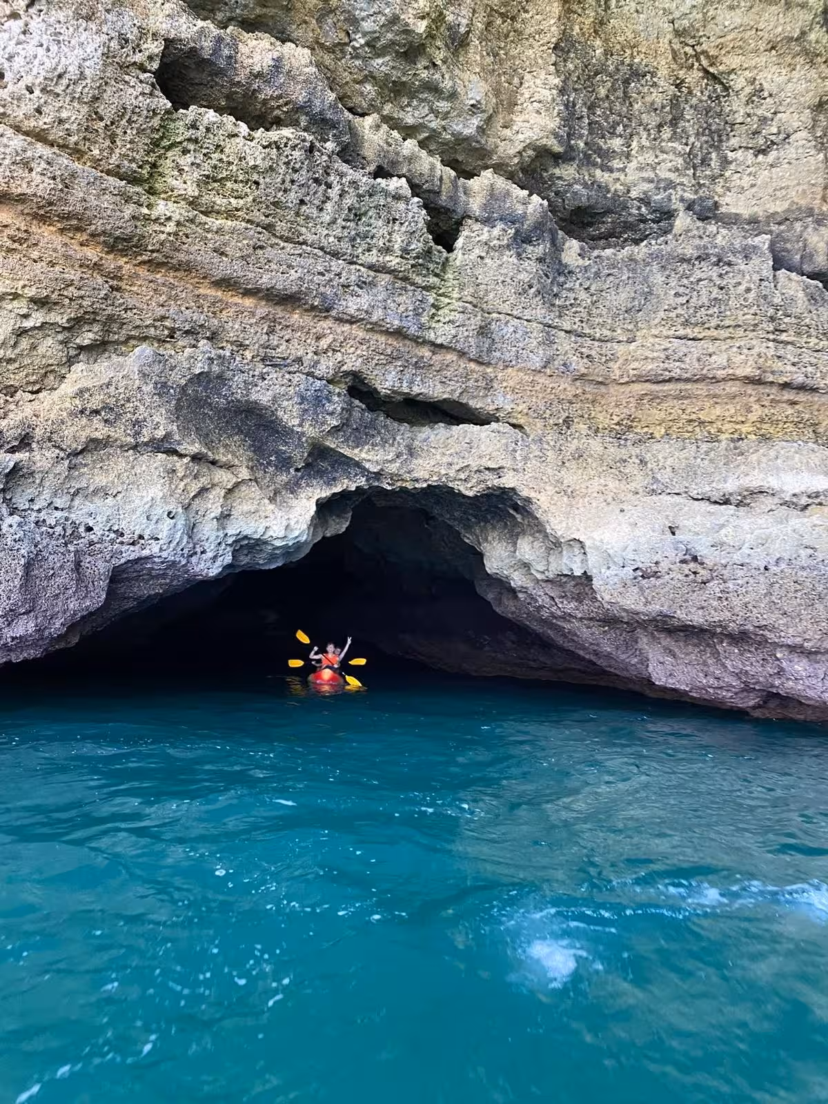 Kayaker entering a sea cave on an Algarve guided kayak tour, paddling in clear turquoise coastal waters