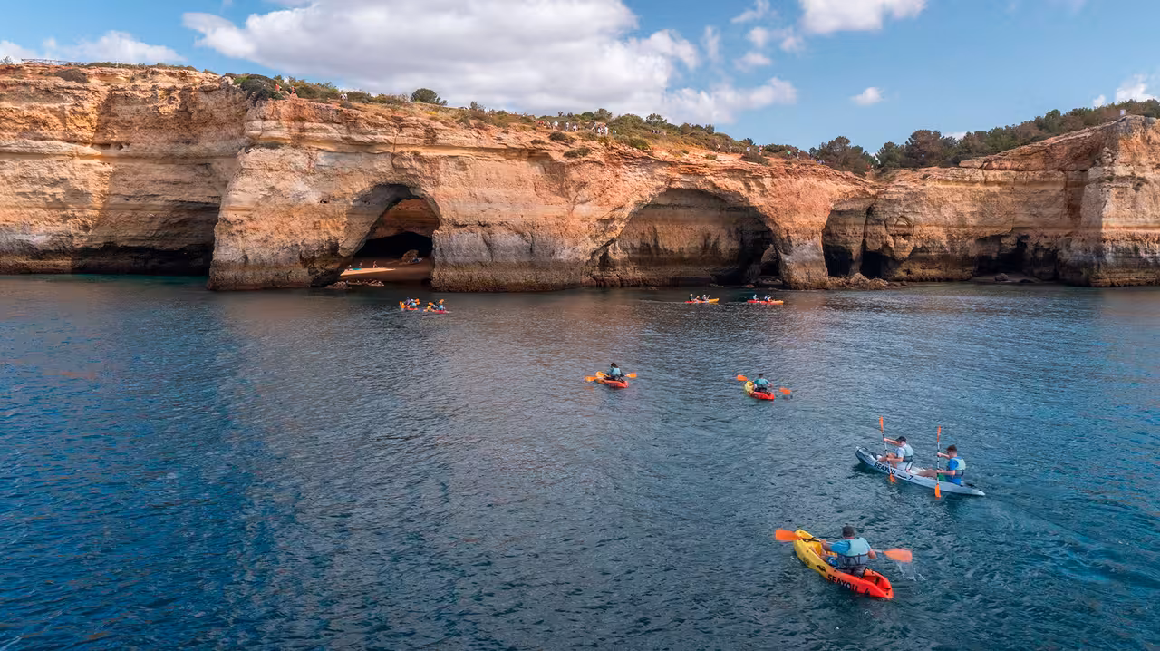 Sea kayaks paddling along Algarve cliffs toward Benagil caves, Portugal, on a guided Benagil Kayak Tour