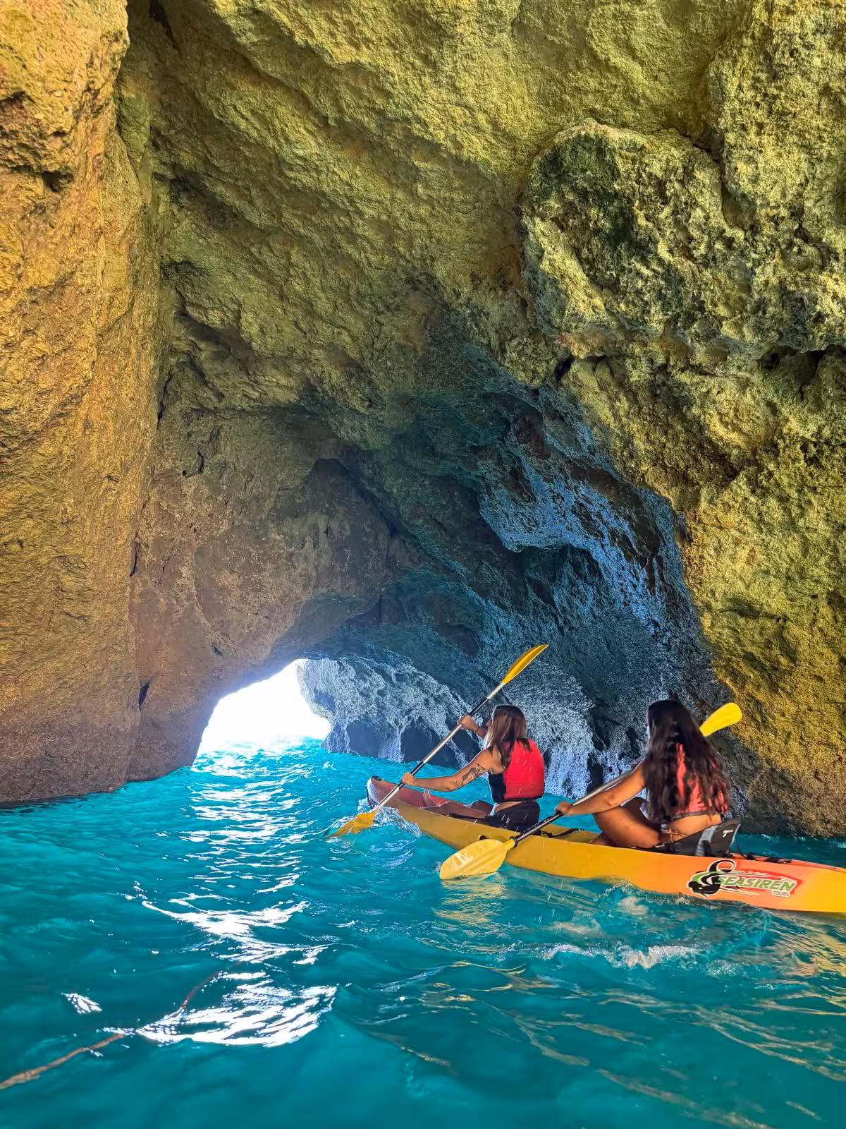 Two friends paddle a yellow kayak through a turquoise sea cave on a guided Benagil kayak tour in the Algarve, Portugal