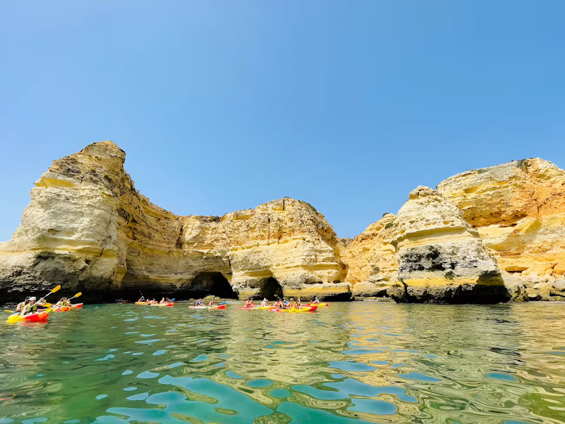 Small group kayaking near stunning Benagil cliffs under clear blue skies on a guided tour in Algarve, Portugal.