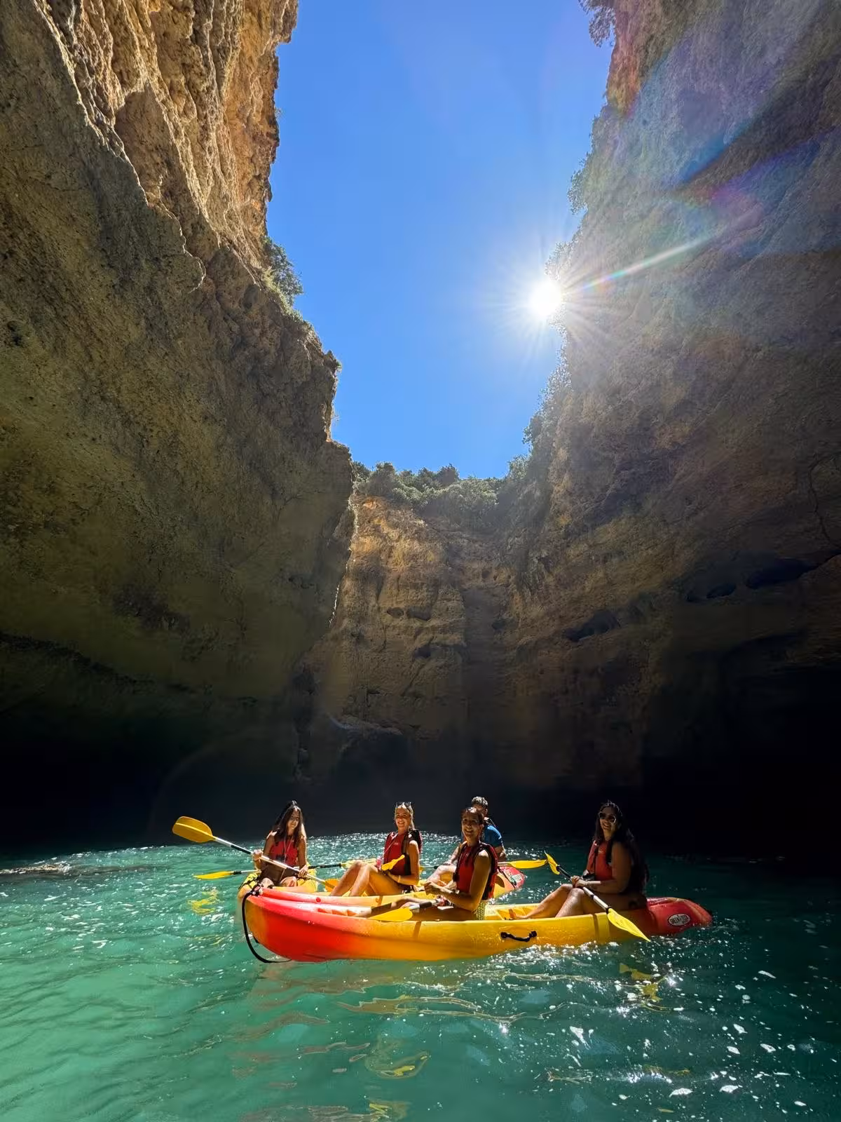 Group of friends kayaking under towering Benagil sea cave cliffs in Algarve, Portugal, on a sunny guided kayak tour