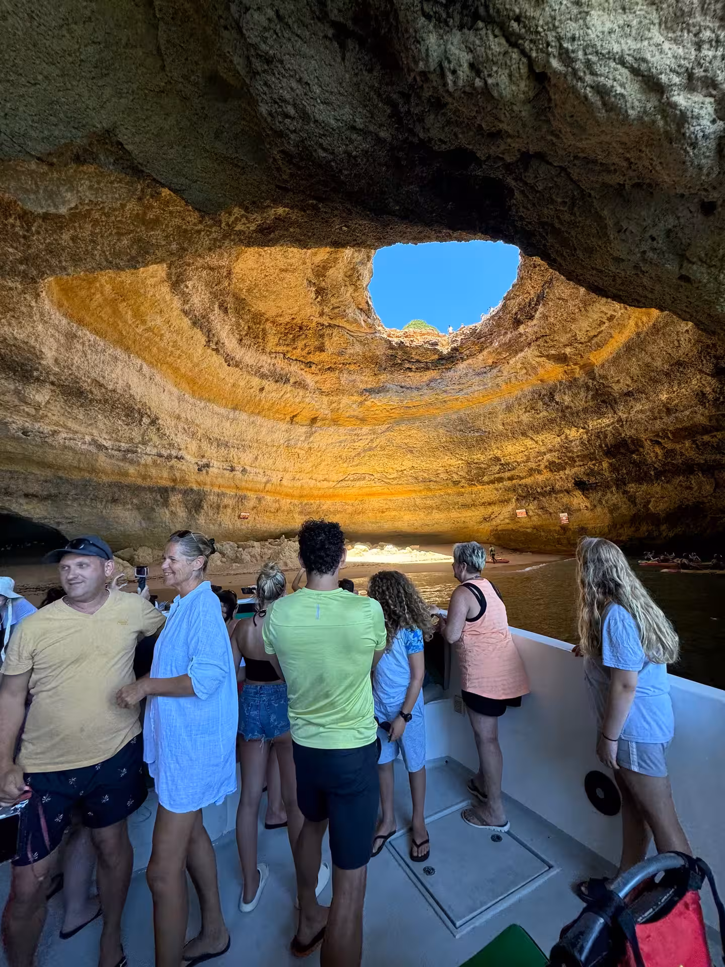 Tourists on a coastal cave boat tour admire sunlight streaming through the Benagil sea cave dome in Algarve, Portugal