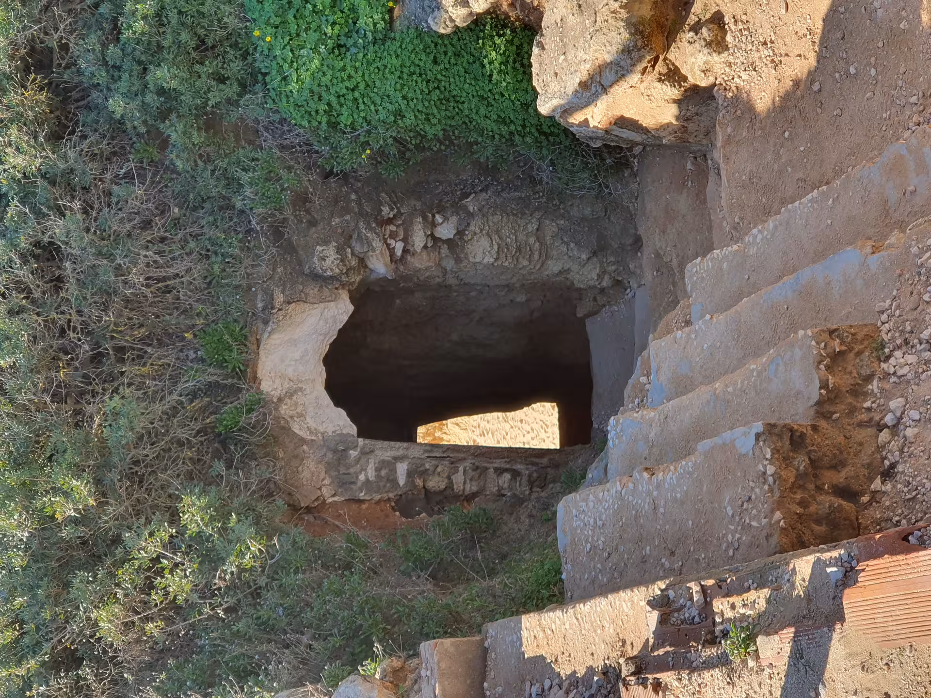 Rocky cliff tunnel with stone steps leading down to a hidden Benagil sea cave viewpoint on the Algarve coast trail