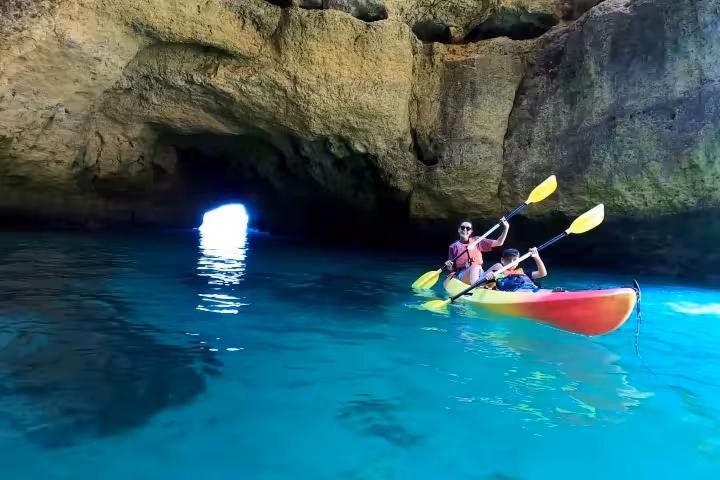 Family in a tandem kayak exploring the illuminated blue waters inside Benagil sea cave on a guided Algarve tour