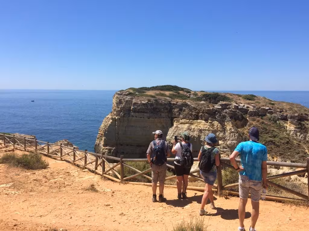 Small group of walkers admiring Benagil sea cliffs and vast Atlantic Ocean views from a wooden viewpoint on Algarve coastal trail
