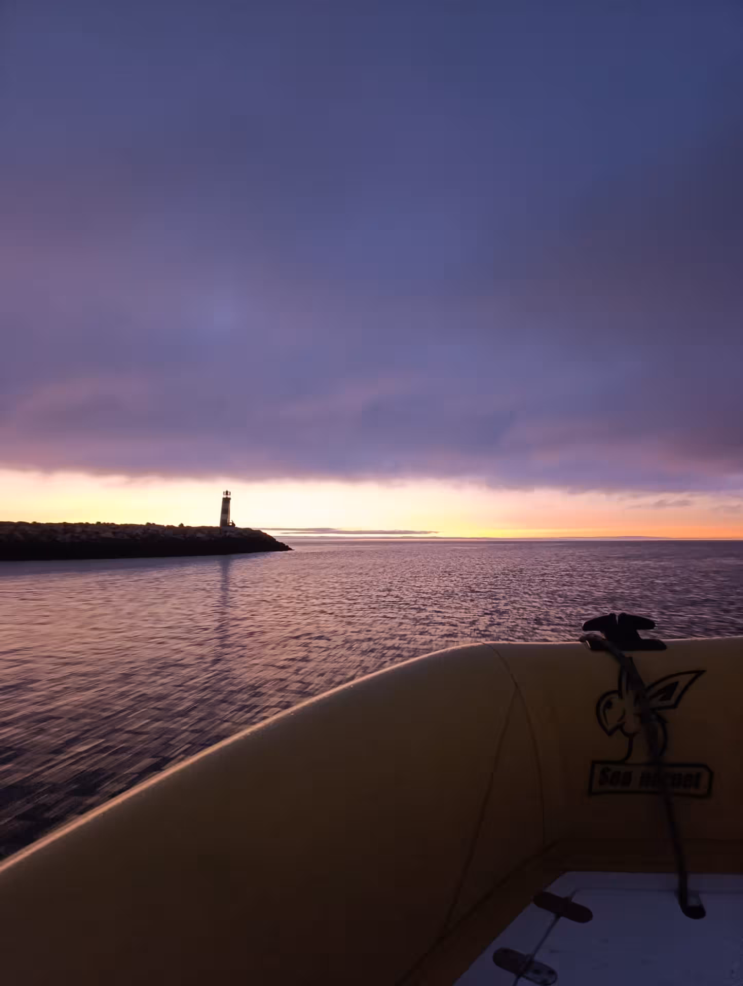 Purple dawn sky and lighthouse silhouette seen from a boat on Benagil Algarve sunrise cave tour