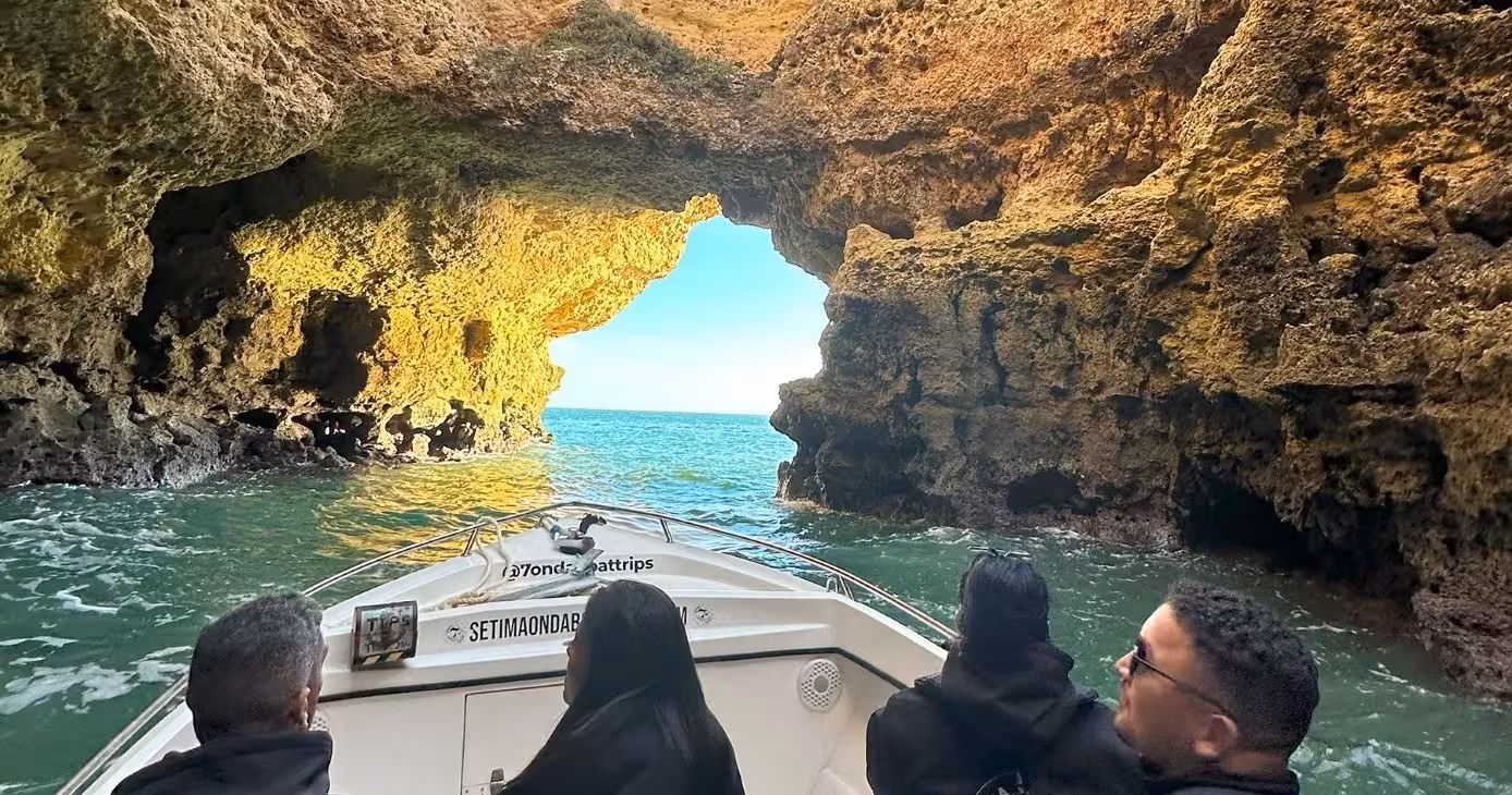 Small boat tour entering Benagil sea cave in Algarve, Portugal, revealing turquoise Atlantic waters at golden hour