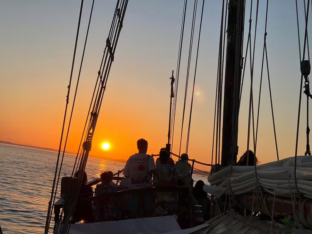 Tourists aboard a sailboat enjoying a vibrant sunset over the ocean during the Benagil sunset cruise experience.