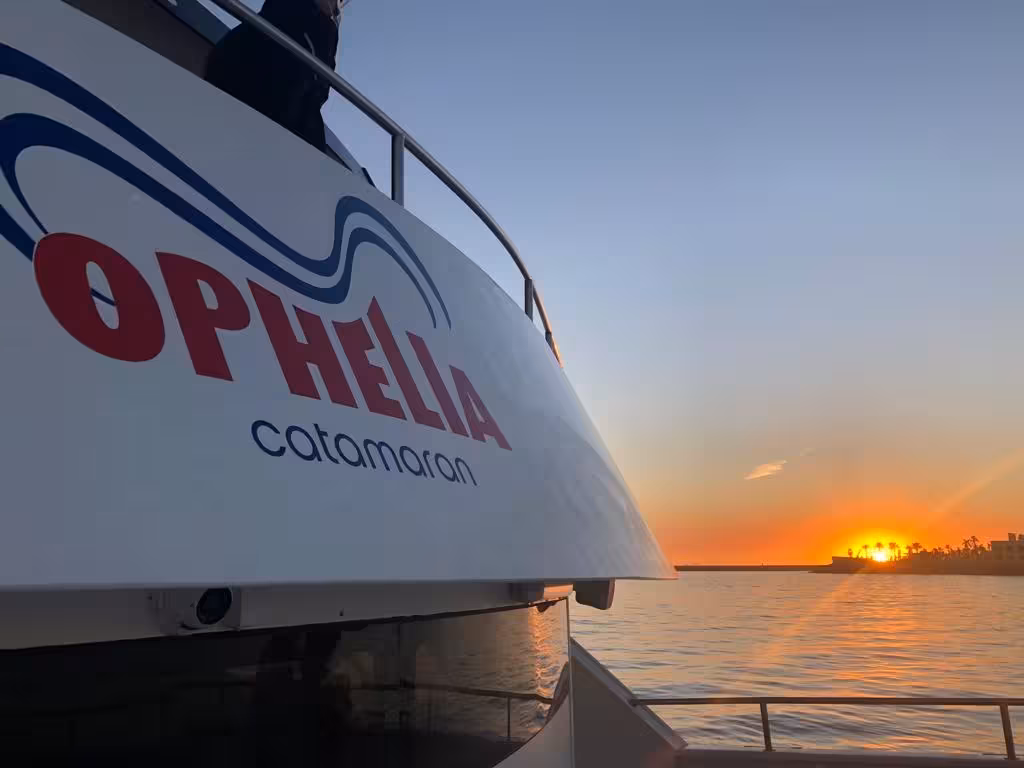 Ophelia catamaran sails into sunset at Benagil, offering a picturesque Algarve coastal experience.