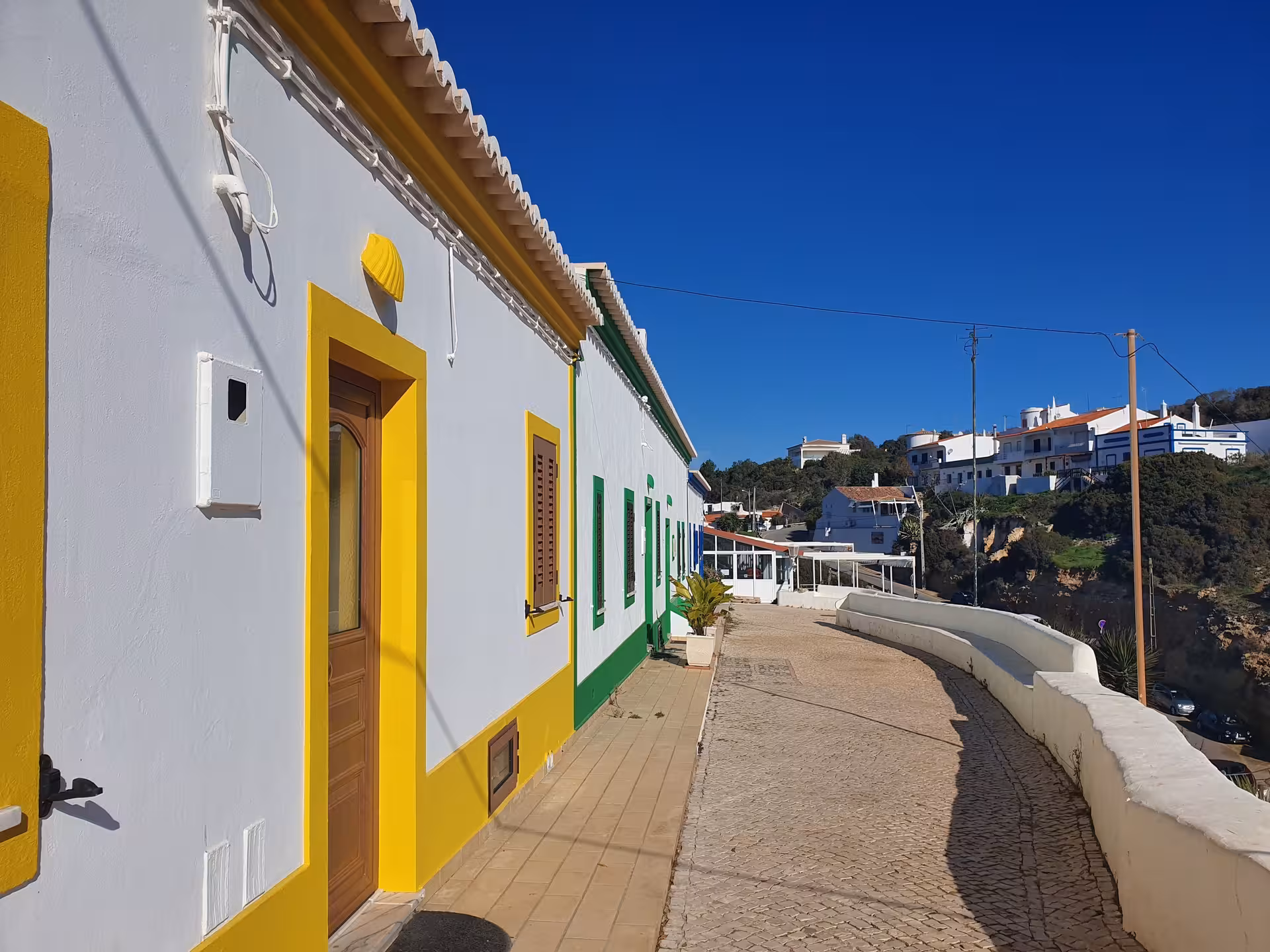 Colorful whitewashed houses with yellow and green trim lining a sunny cobbled street in Benagil village, Algarve Portugal