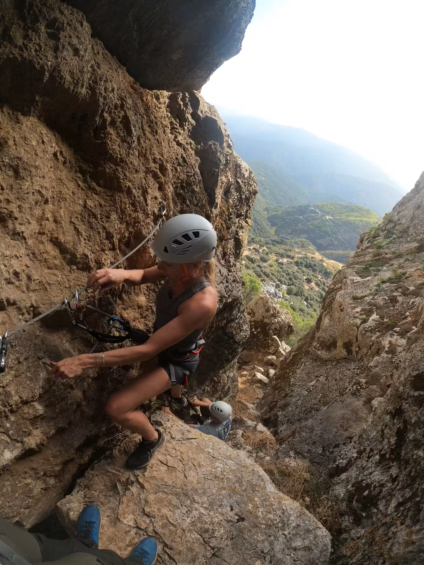 Climber navigating rugged terrain on Benalauría Via Ferrata with expansive views of the Costa del Sol landscape.