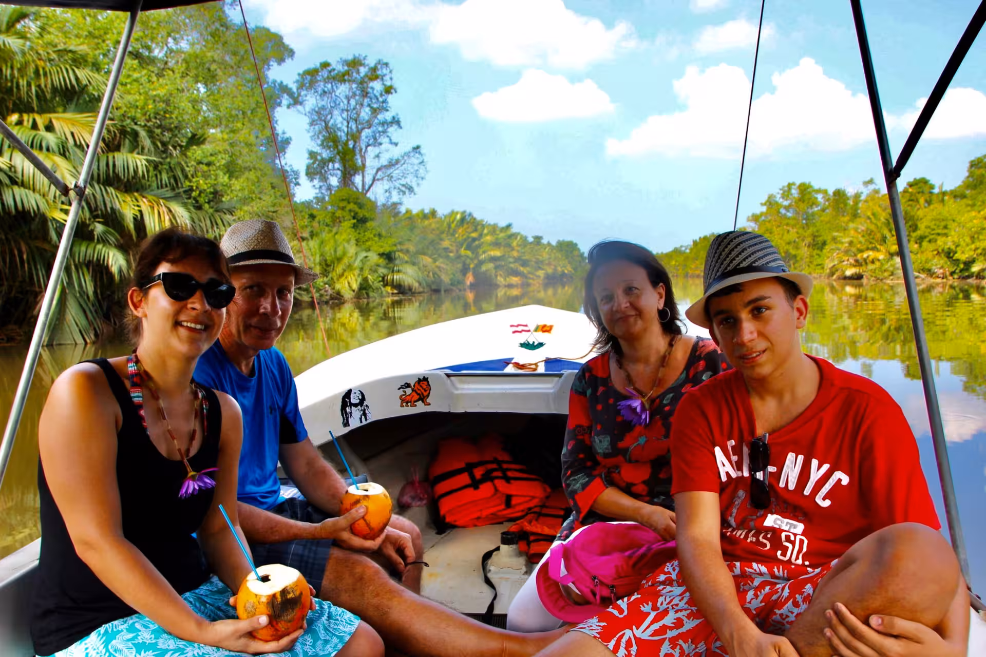 Tourists relaxing on a Bentota River safari boat with fresh coconuts, cruising through Sri Lanka mangroves