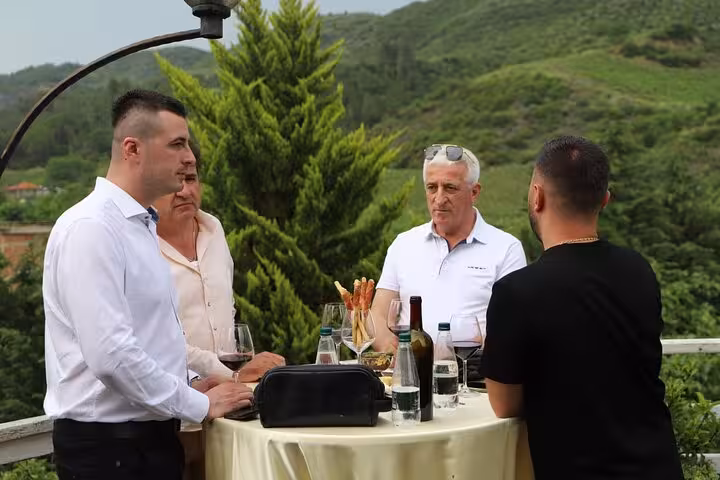 Group enjoying wine tasting at a vineyard with lush green hills in the background during Berat 4x4 off-road tour.
