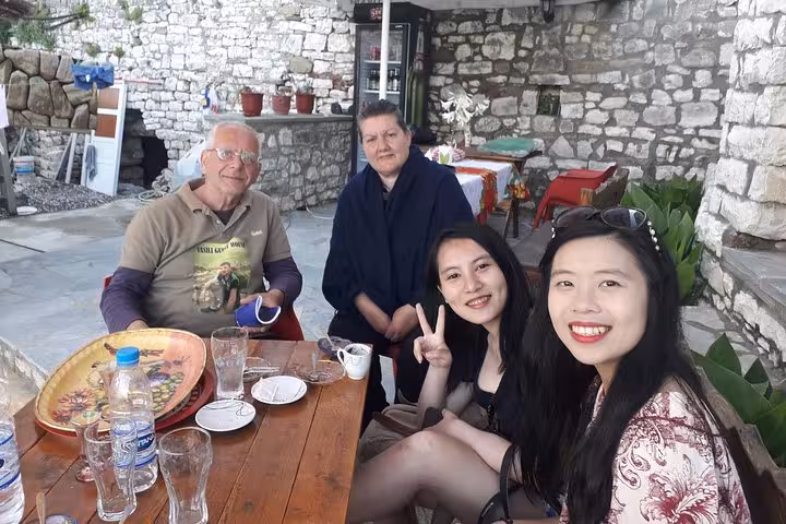 Guests relaxing after a traditional Albanian cooking class in Berat, seated at a rustic outdoor table with local hosts.