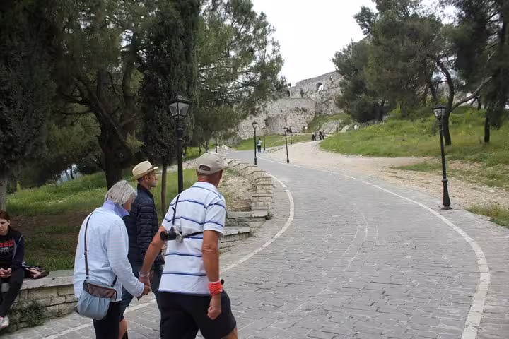 Visitors walk through a scenic, tree-lined path towards the ancient Berat Castle during a historical walking tour.