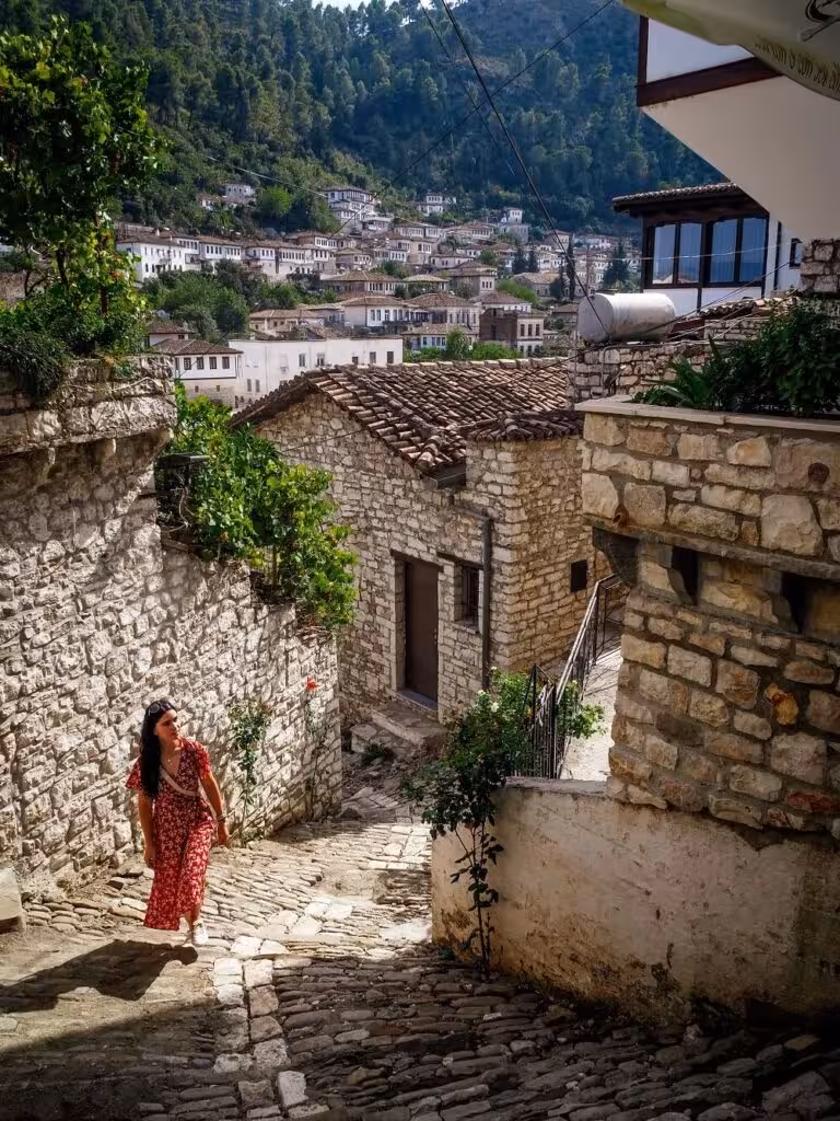 Traveler exploring Berat's charming cobblestone streets lined with traditional stone houses and lush greenery.