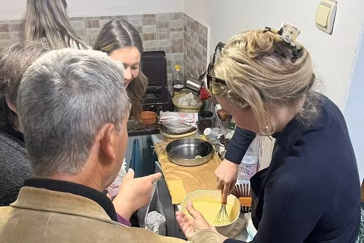 Enthusiastic group learns to whisk and prepare Albanian dishes in a cozy kitchen during Berat cooking class.