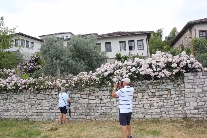 Visitors photograph beautiful stone houses and blooming flowers in Berat's historic district, Albania.