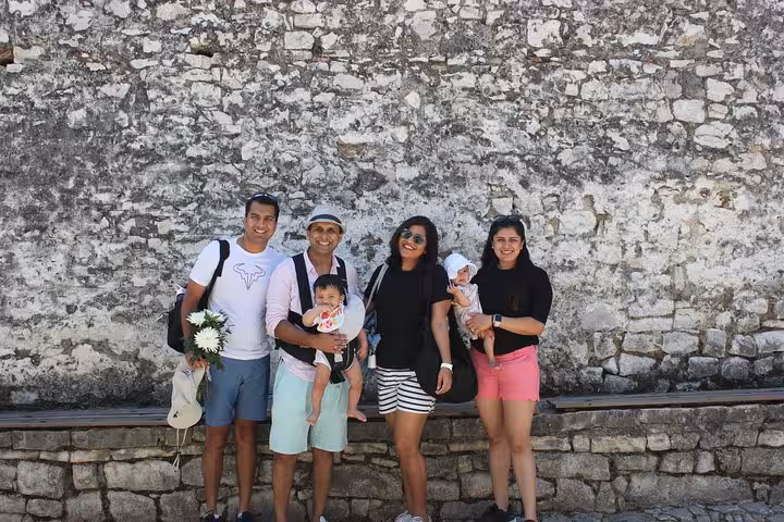 Group of tourists enjoying a historical walking tour in Berat, posing against an ancient stone wall.