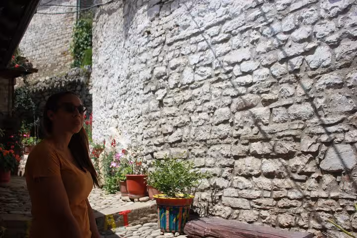 Visitor admires the rustic charm of Berat's stone alleyways, surrounded by vibrant potted plants.