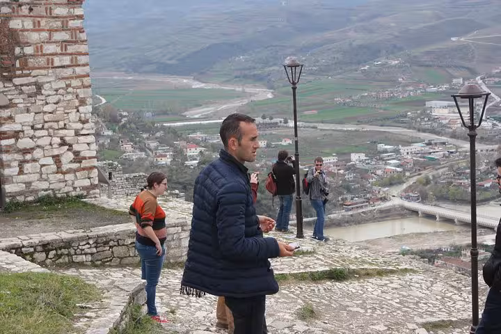 Tourists explore the ancient stone pathways of Berat, Albania, with panoramic views of the city and surrounding hills.