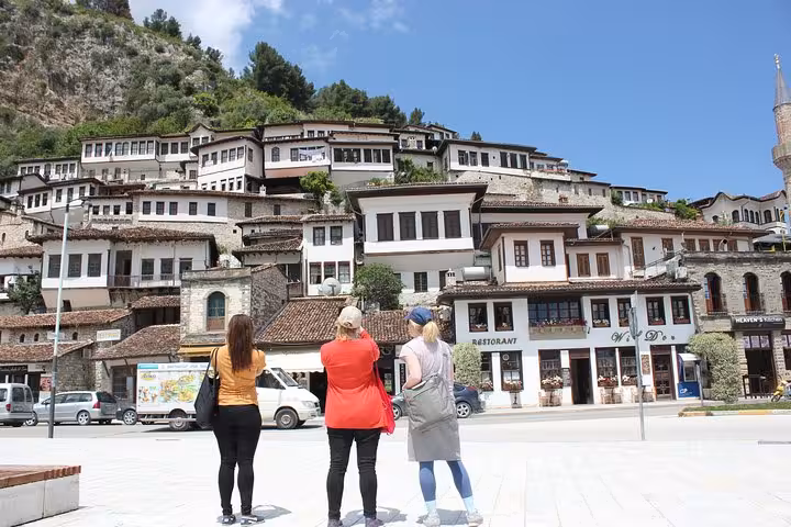 Small group marvels at Berat's picturesque hillside houses, experiencing a cultural walking tour on a sunny day.