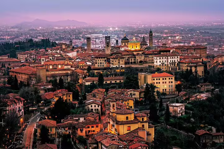 Twilight panoramic view of Bergamo Alta with glowing medieval towers and terracotta roofs on a private 2.5-hour walking tour