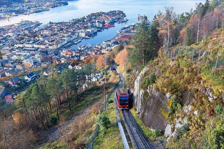 Red funicular ascending Mount Fløyen with panoramic aerial view of Bergen city and harbor below