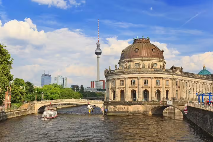 Bode Museum and Berlin TV Tower along the Spree River with a tourist boat passing under a stone bridge