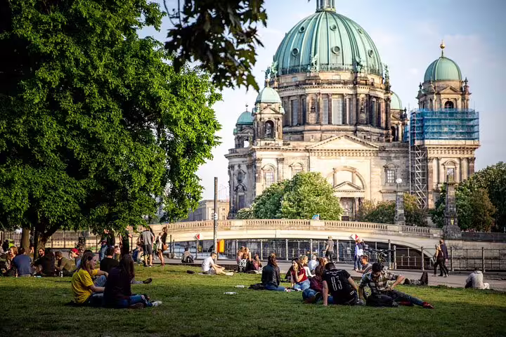 People relaxing on grass with Berlin Cathedral's green copper domes in background on sunny day