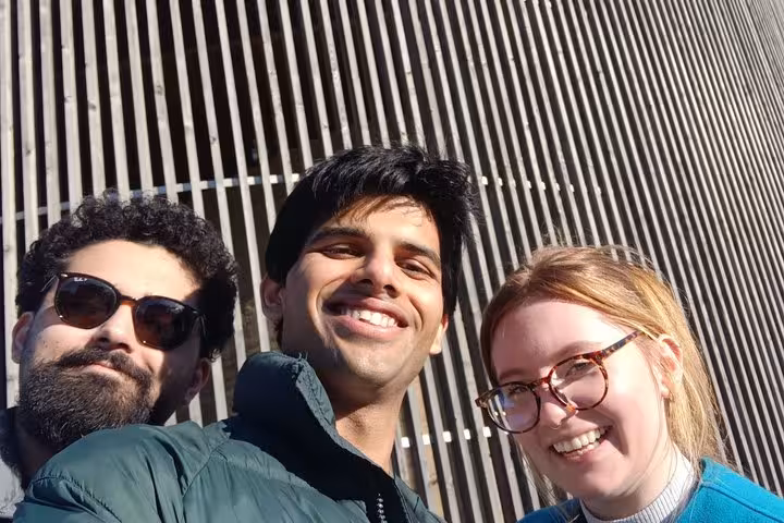 Three smiling people posing together outdoors in front of a striped wall in Berlin