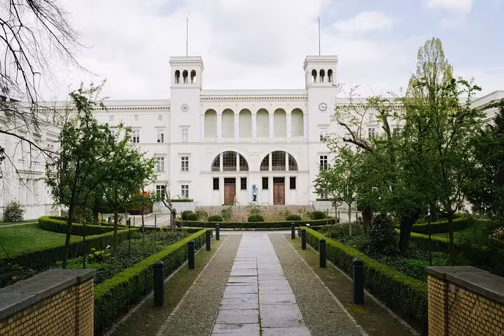White neoclassical building with arched entrance, twin towers, and manicured garden pathway in Berlin