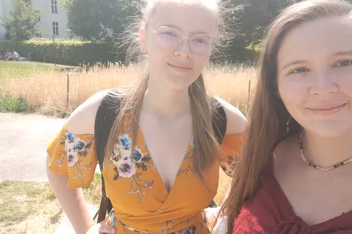 Two young women smiling outdoors in a sunny Berlin park during a walking tour