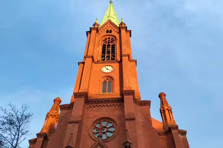 Red brick Gothic church tower with clock and green spire in Berlin at dusk