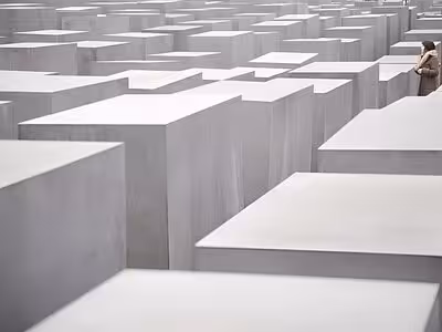 Rows of grey concrete slabs at the Holocaust Memorial in Berlin with a visitor standing among them