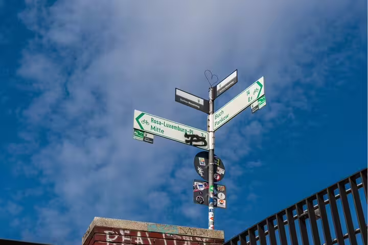 Green bicycle route signs pointing to Rosa-Luxemburg-Platz and Mitte on a street pole in Berlin