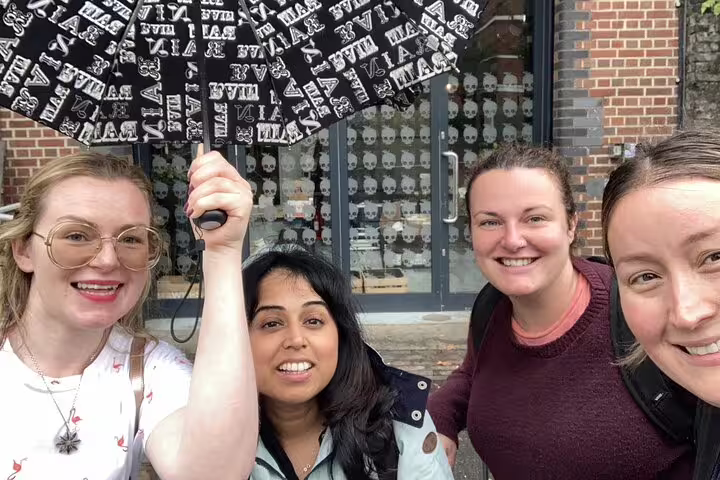 Four women smiling on Bermondsey walking tour, one holding a black patterned umbrella outside a brick building