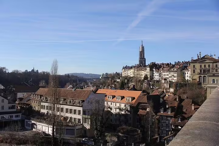 Panoramic view of Bern old town with cathedral spire and terracotta rooftops under blue sky, Switzerland