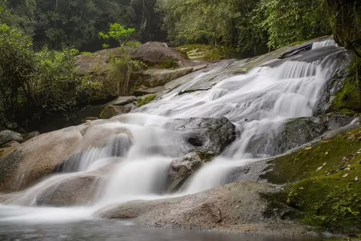 Cascading waterfall amidst lush greenery on Bertioga's Coastal Trail, showcasing serene natural beauty.