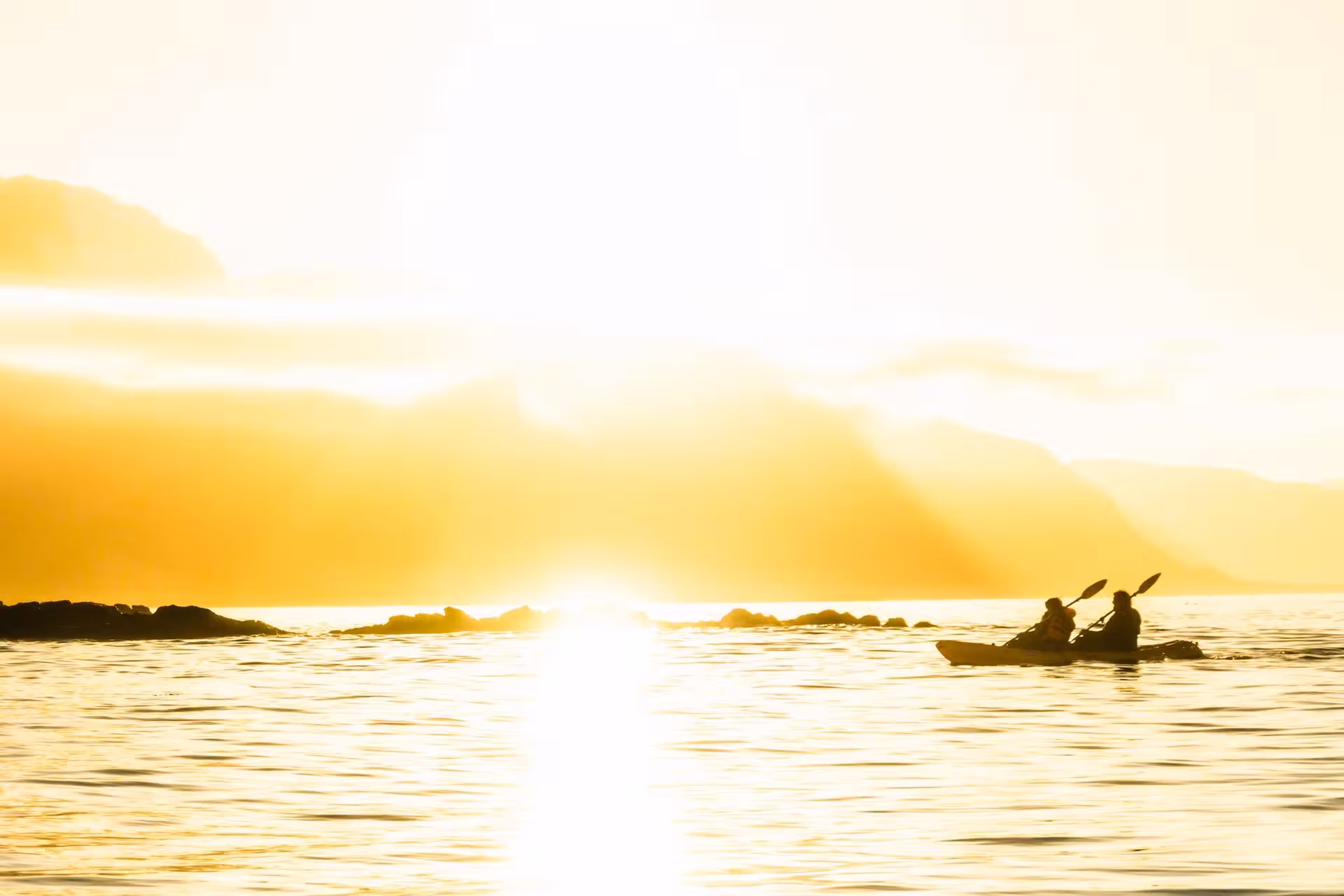 Kayakers silhouetted against a golden sunrise on Berufjörður, experiencing the serene beauty of Iceland's East Fjords.