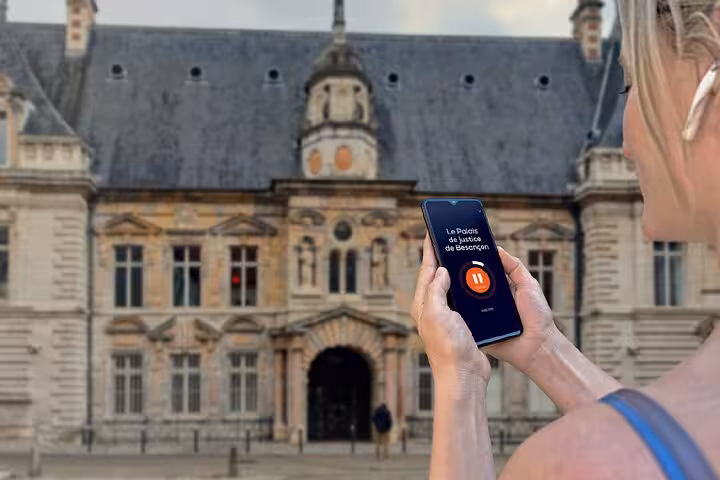 Woman holding smartphone with audio tour app at Palais de Justice de Besançon, France