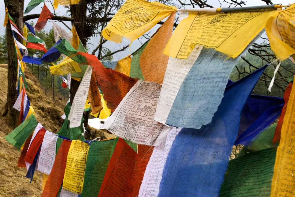 Colorful prayer flags fluttering in the wind against a mountainous backdrop in Bhutan, enhancing spiritual journeys.