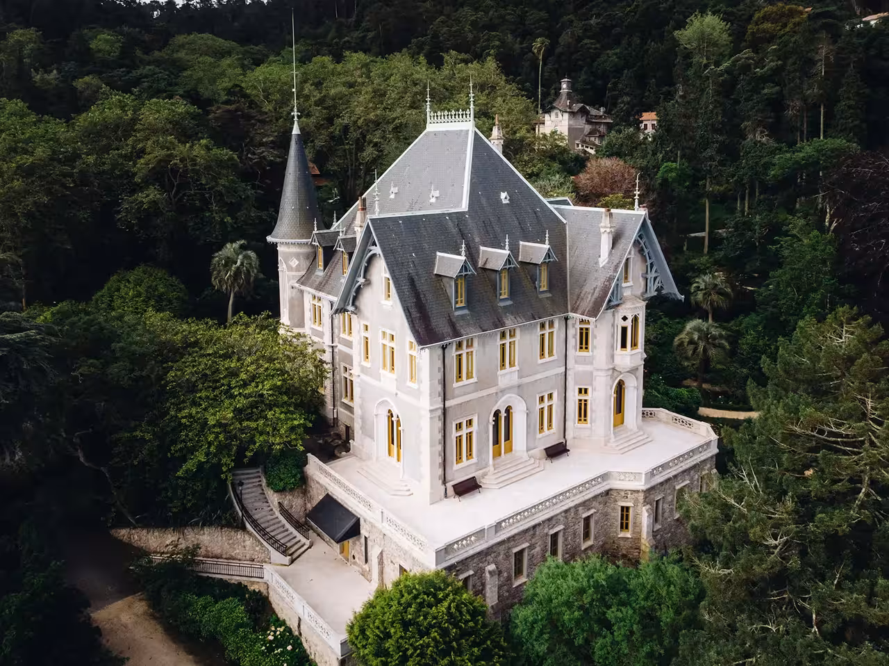 Aerial view of Biester Palace in Sintra, a stunning Neo-Gothic mansion with turrets surrounded by lush green forest.